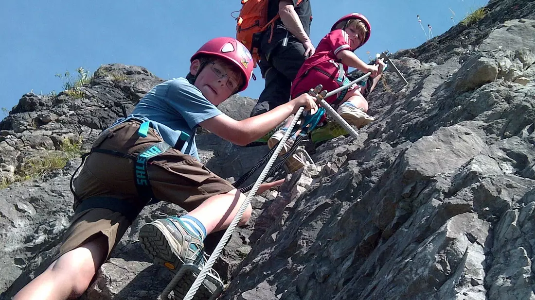 Bergführer Patrick Jost erklärt den Kindern Julius (9) und Jakob (6) wie man sich in einem Klettersteig richtig verhält. - Bild: Bad Hindelang Tourismus