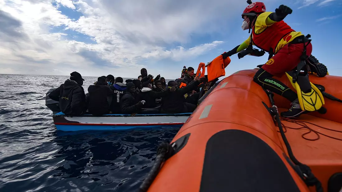 Mehrere Migranten sitzen in einem Boot im Mittelmeer während Rettungskräfte versuchen ihnen zu helfen. - Bild: Antonio Sempere/EUROPA PRESS/dpa