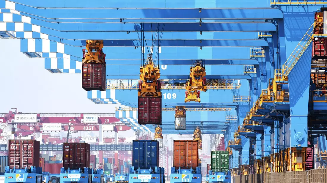 Portalkräne bewegen Container auf Transporter in einem Hafen in Qingdao in der ostchinesischen Provinz Shandong. - Bild: Uncredited/CHINATOPIX/dpa