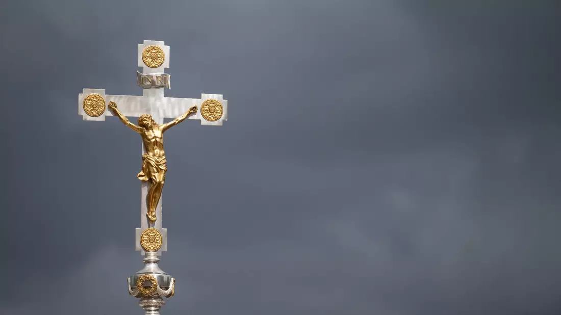 Dunkle Wolken über einem Kruzifix: Immer mehr Menschen nehmen Abstand von der Katholischen Kirche. - Bild: Marijan Murat/dpa
