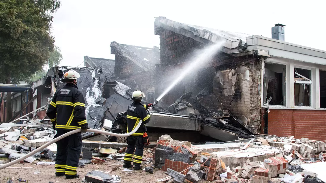 Polizisten stehen hinter einem Metallbehälter. Trümmerteile sollen bei dem Brand Hunderte Meter weit geflogen sein.  - Bild: Daniel Bockwoldt/dpa