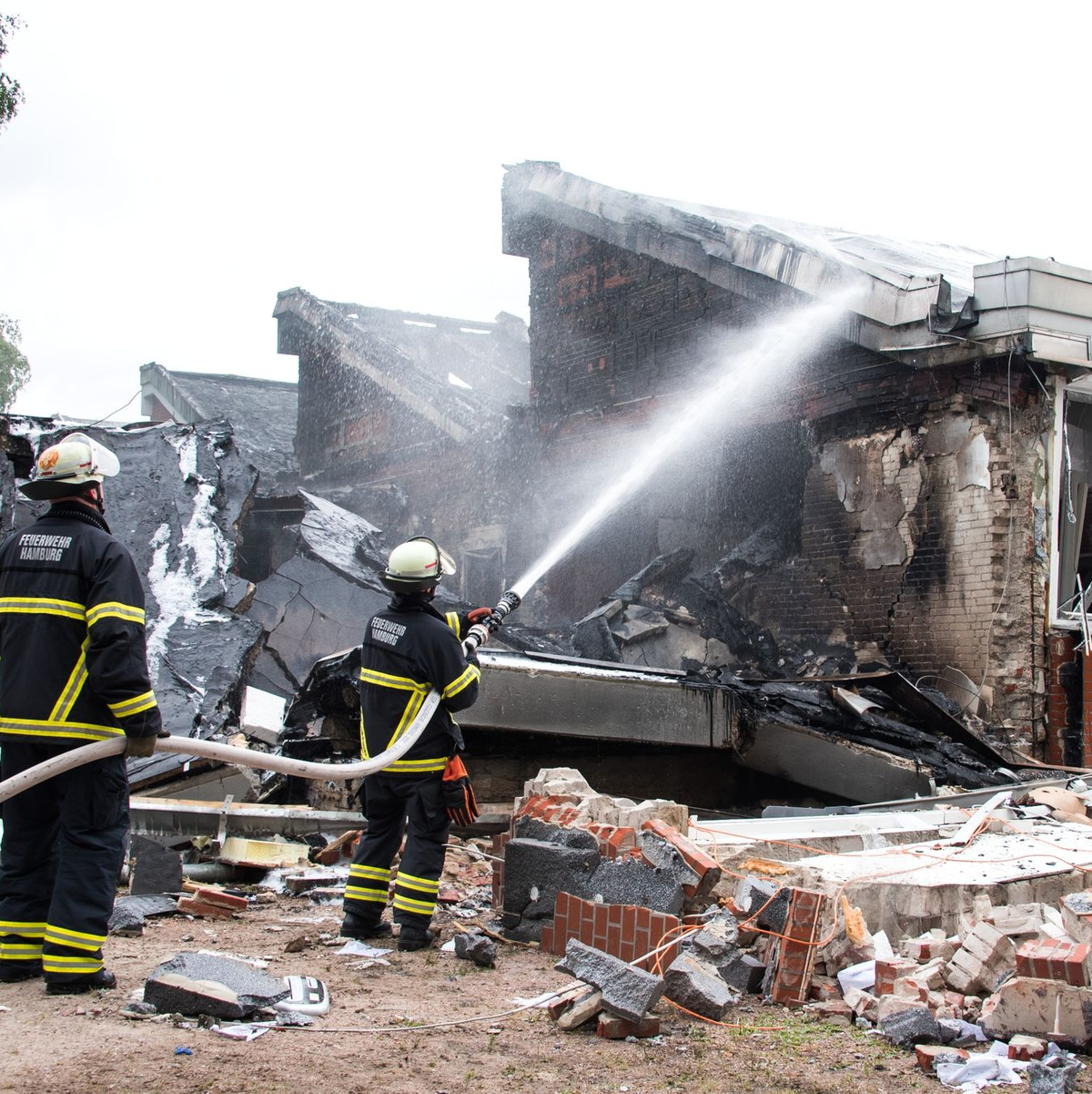 Polizisten stehen hinter einem Metallbehälter. Trümmerteile sollen bei dem Brand Hunderte Meter weit geflogen sein.  - Foto: Daniel Bockwoldt/dpa