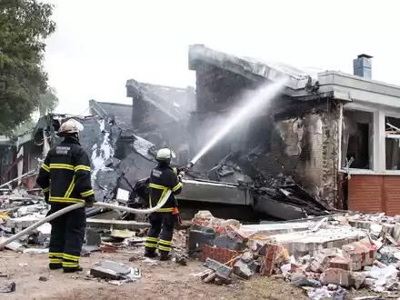 Polizisten stehen hinter einem Metallbehälter. Trümmerteile sollen bei dem Brand Hunderte Meter weit geflogen sein. - Foto: Daniel Bockwoldt/dpa