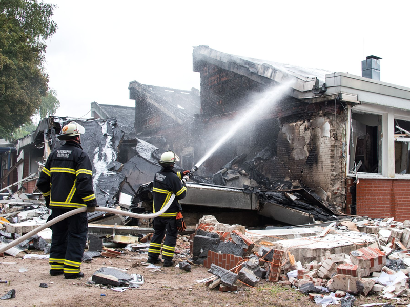 Polizisten stehen hinter einem Metallbehälter. Trümmerteile sollen bei dem Brand Hunderte Meter weit geflogen sein.  - Foto: Daniel Bockwoldt/dpa