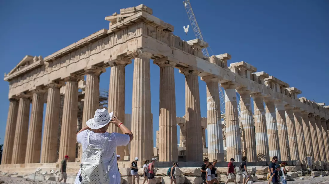 Touristen spazieren auf dem Lycabettus-Hügel, während der Himmel über Athen mit dem antiken Akropolis-Hügel im Hintergrund infolge von Saharastaub eingetrübt ist. - Bild: Petros Giannakouris/AP/dpa