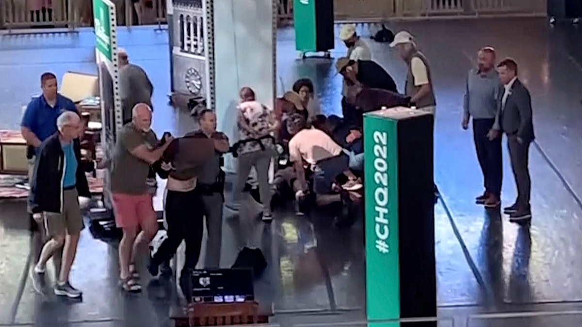 Menschen kümmern sich um den verletzten Rushdie, während ein Mann von der Bühne eskortiert wird. (Aufnahme kurz nach dem Angriff) - Foto: Uncredited/AP/dpa