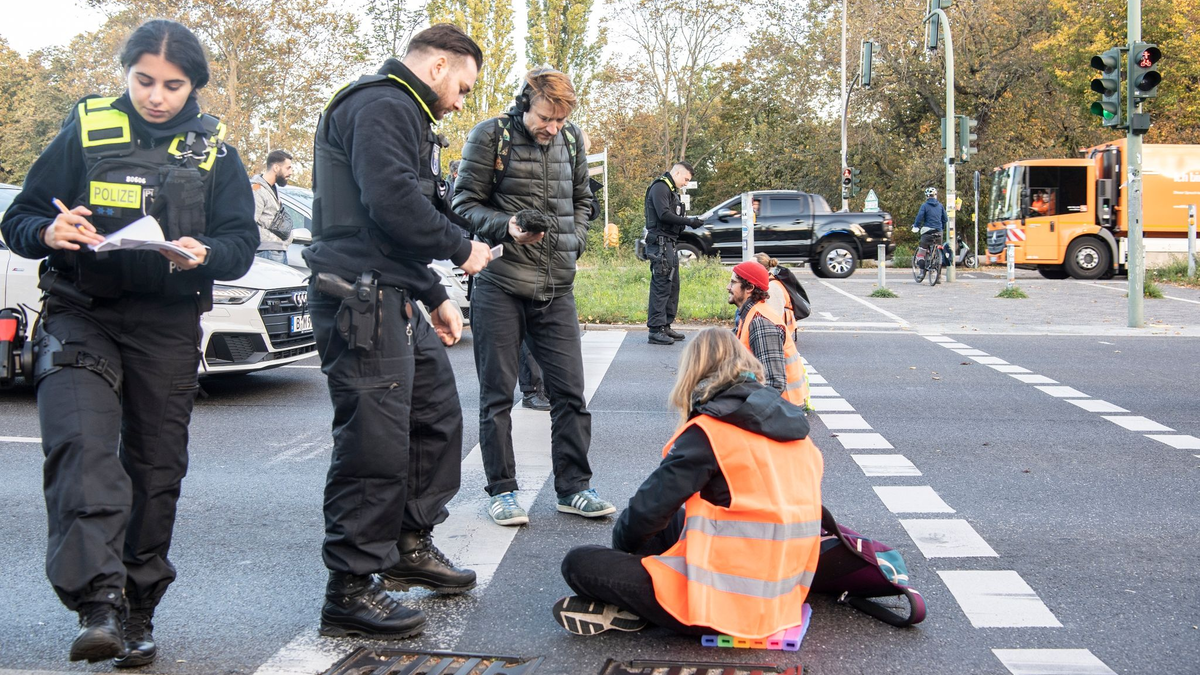 Ein Verkehrsteilnehmer zieht bei einer Blockade der Letzten Generation auf der Autobahn 100 eine Aktivistin von der Straße. Erneut hat die Klimaaktivistengruppe an zahlreichen Stellen in Berlin Straßen blockiert. - Foto: Paul Zinken/dpa