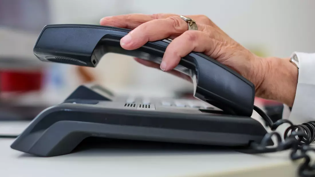 Eine Frau nimmt einen Telefonhörer in die Hand. - Bild: Jan Woitas/dpa