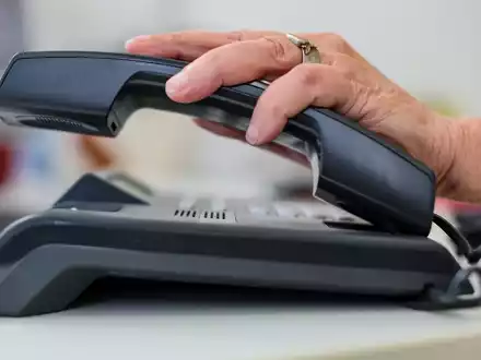 Eine Frau nimmt einen Telefonhörer in die Hand. - Foto: Jan Woitas/dpa