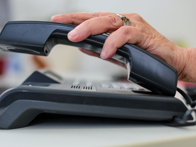 Eine Frau nimmt einen Telefonhörer in die Hand. - Foto: Jan Woitas/dpa