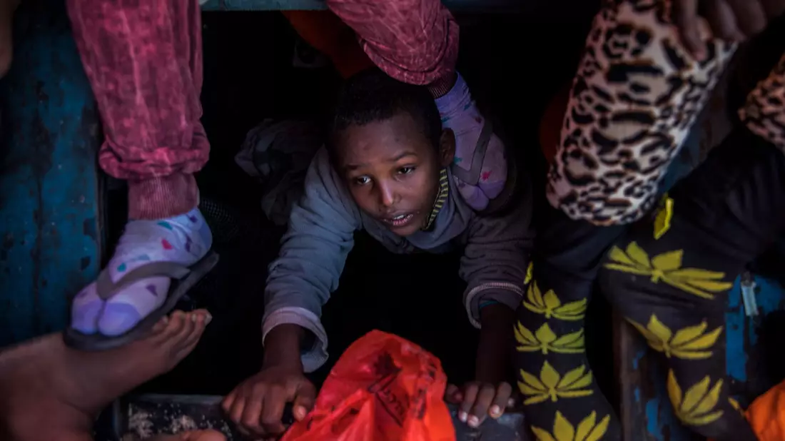 Ein Flüchtlingskind aus Eritrea versucht an der Küste zu Libyen, an Bord eines überfüllten Holzbootes hinaufzuklettern. - Bild: Santi Palacios/AP/dpa