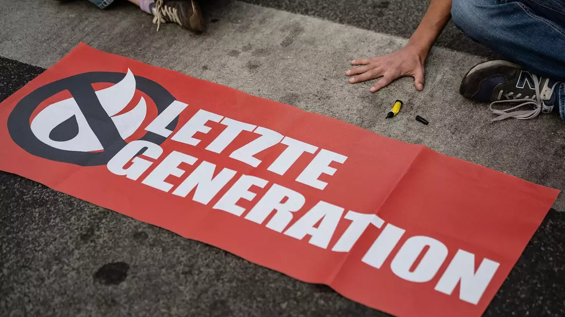 Ein Aktivist der Gruppe «Letzte Generation», der seine Hand selbst auf der Straße festgeklebt hat, blockiert eine Kreuzung in Göttingen. - Bild: Swen Pförtner/dpa