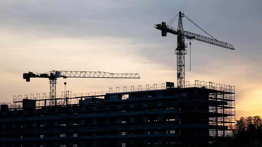 Kräne stehen hinter dem Rohbau für ein Bürogebäude auf einer Baustelle. Die Flaute am Bau hat sich auch im März fortgesetzt. - Bild: Hendrik Schmidt/dpa