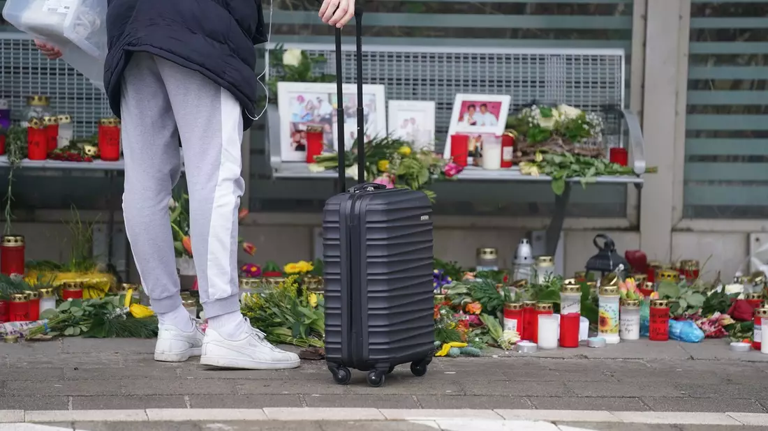 Eine Reisende schaut sich die Blumen, Kerzen und verschiedene Bilder im Wartehäuschen am Bahnhof zum Gedenken an die Opfer der Messerattacke an. - Bild: Marcus Brandt/dpa