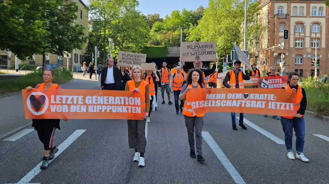 Aktivistinnen und Unterstützer der Gruppierung Letzte Generation demonstrieren in Stuttgart mit Transparenten. - Bild: Andreas Rosar/dpa