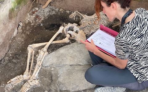Eine Frau sitzt vor einem Skelett im Archäologiepark Pompeji. - Foto: -/Archäologiepark Pompeji/dpa