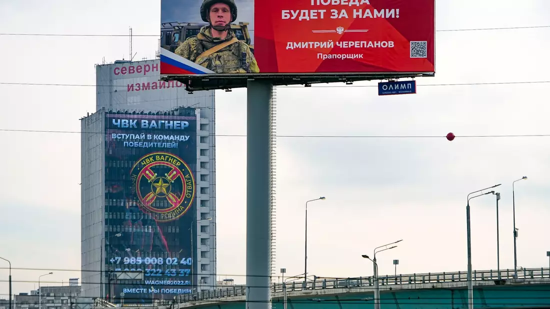 Ein Werbeschild, auf dem für das Militärunternehmen Wagner (hinten) geworben wird und auf dem zu lesen ist «Schließen Sie sich dem Team der Sieger an». - Bild: Alexander Zemlianichenko/AP/dpa
