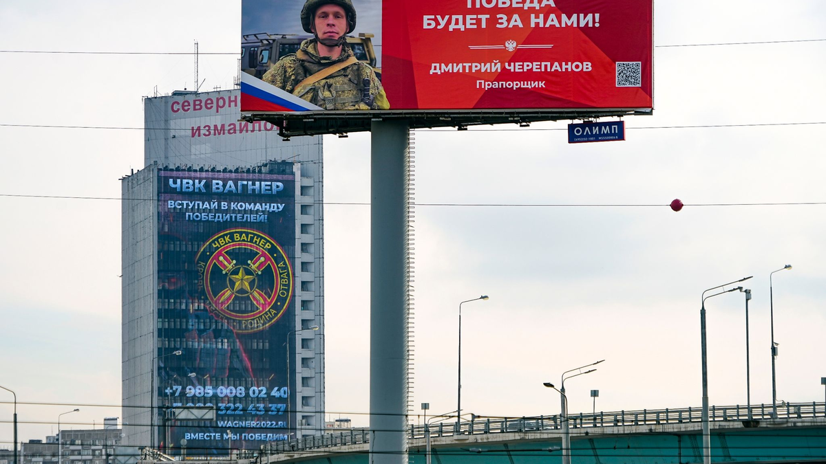 Ein Werbeschild, auf dem für das Militärunternehmen Wagner (hinten) geworben wird und auf dem zu lesen ist «Schließen Sie sich dem Team der Sieger an». - Foto: Alexander Zemlianichenko/AP/dpa