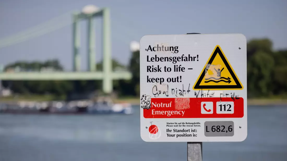Ein Schild am Rheinufer weist auf die Gefahren beim Schwimmen im Fluss hin. - Bild: Rolf Vennenbernd/dpa