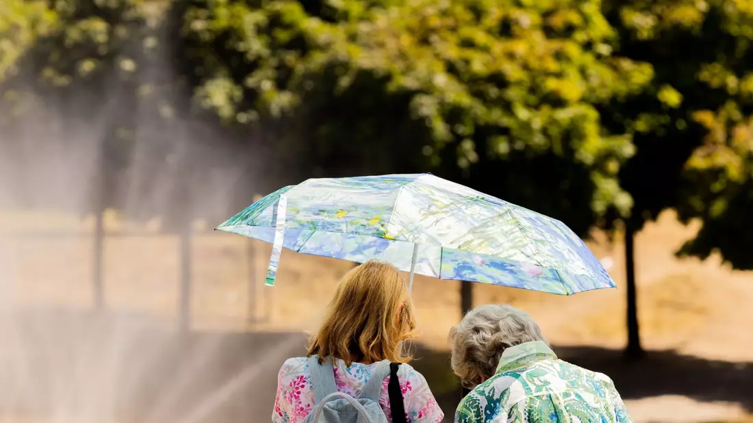 Zwei Frauen schützen mit einem Regenschirm vor der Sonne. - Bild: Rolf Vennenbernd/dpa