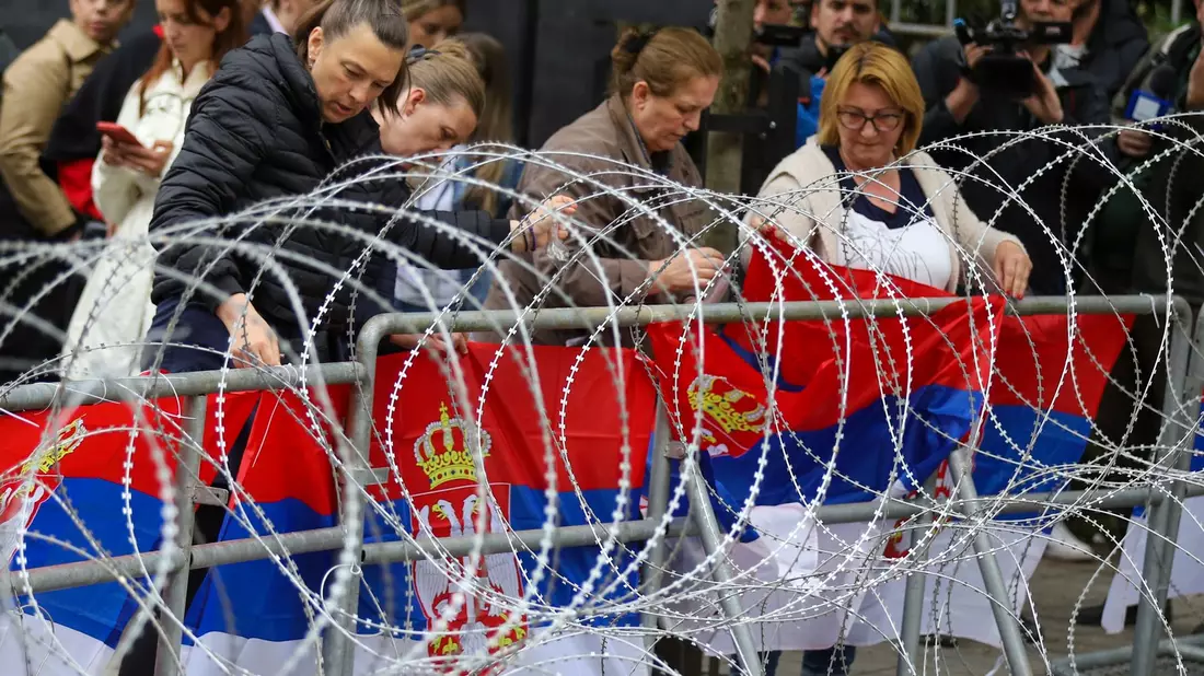 Frauen befestigen serbische Flaggen an einem Zaun vor dem Rathaus während einer Demonstration in der Stadt Zvecan im Norden des Kosovo. - Bild: Bojan Slavkovic/AP