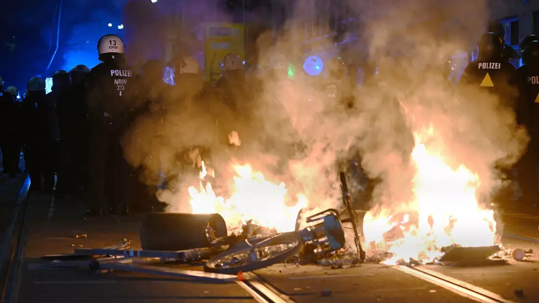 Polizisten hinter einer brennenden Barrikade. - Bild: Robert Michael/dpa