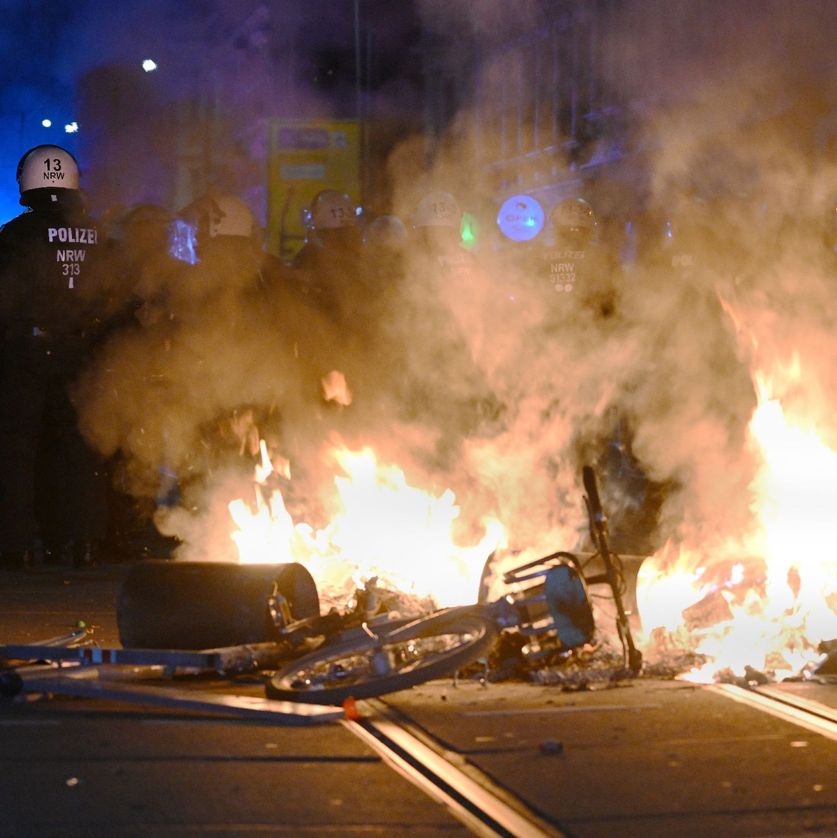 Polizisten hinter einer brennenden Barrikade. - Foto: Robert Michael/dpa