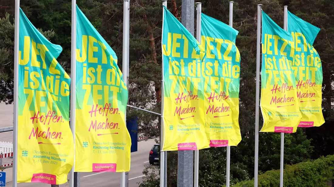 Fahnen wehen vor dem Messezentrum in Nürnberg, wo heute der 38. Evangelische Kirchentag beginnt. - Bild: Daniel Karmann/dpa