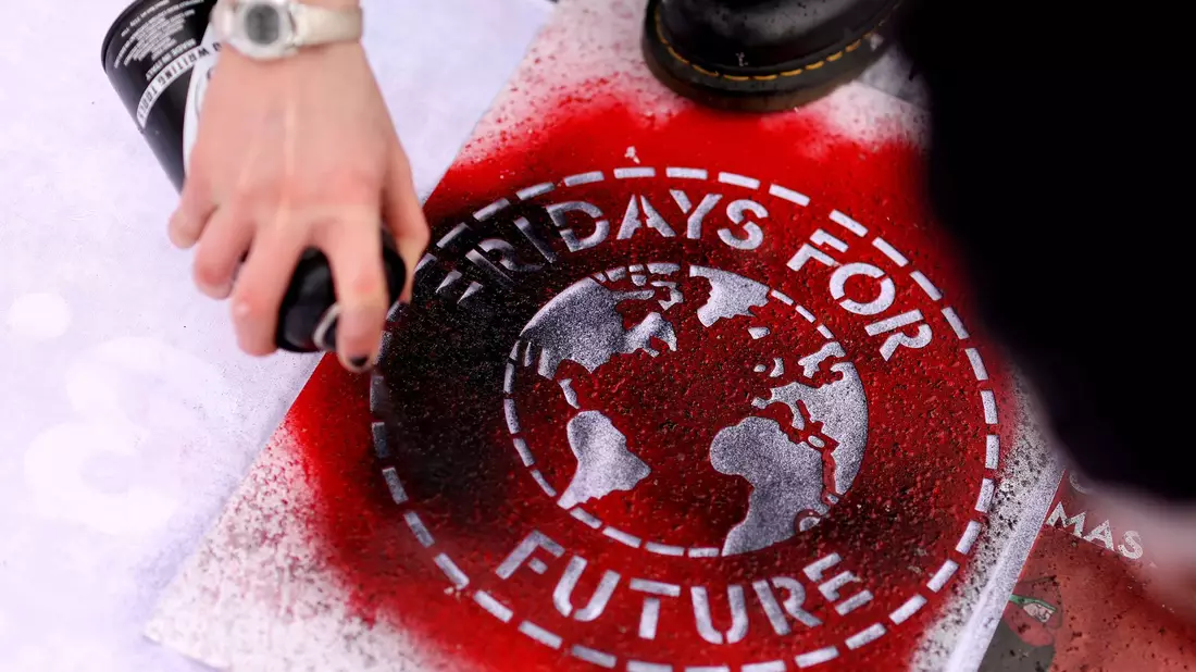 Eine Klimaaktivistin sprüht während einer Kundgebung ein Logo der Bewegung Fridays For Future auf ein Transparent. - Bild: Ronny Hartmann/dpa-Zentralbild/dpa