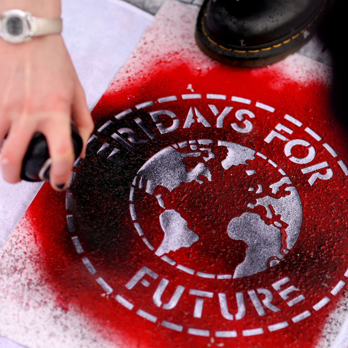 Eine Klimaaktivistin sprüht während einer Kundgebung ein Logo der Bewegung Fridays For Future auf ein Transparent. - Foto: Ronny Hartmann/dpa-Zentralbild/dpa