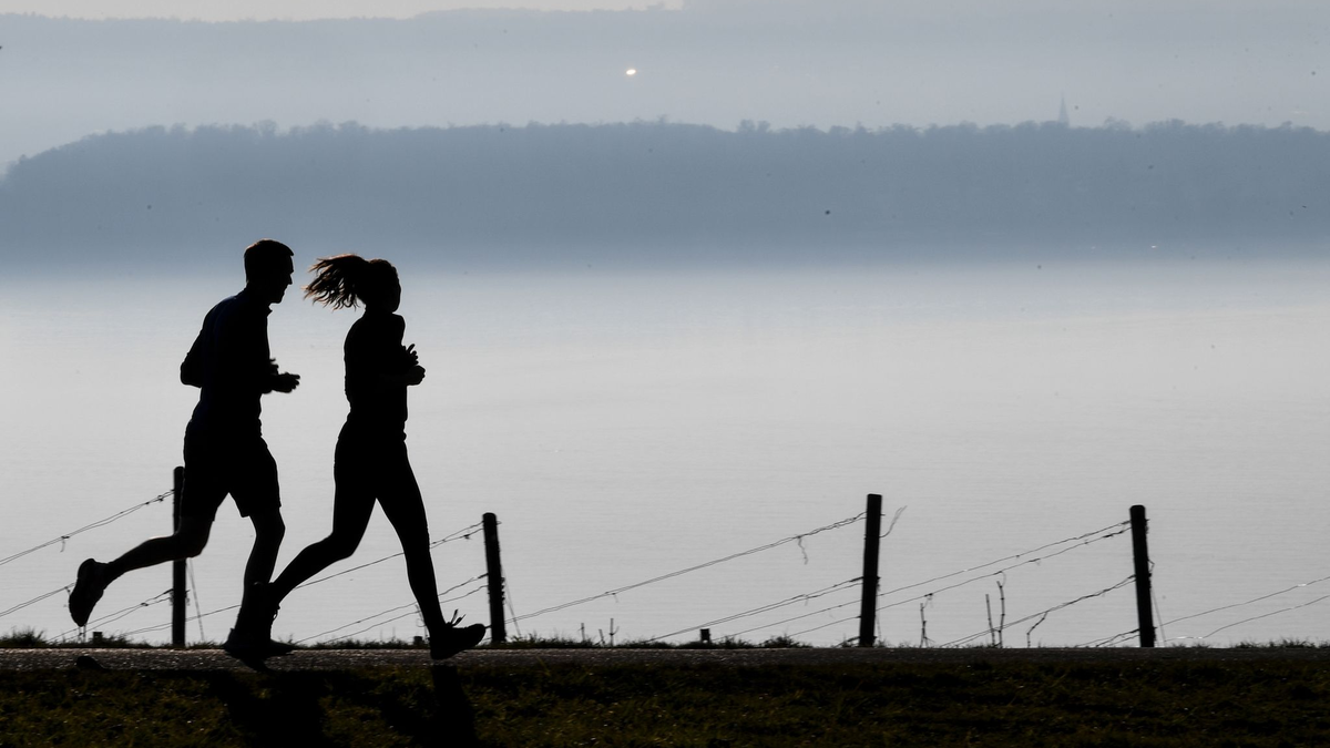 Jogger laufen in Richtung Meersburg, im Dunst dahinter liegt die Stadt Konstanz am Bodensee. - Foto: Felix Kästle/dpa