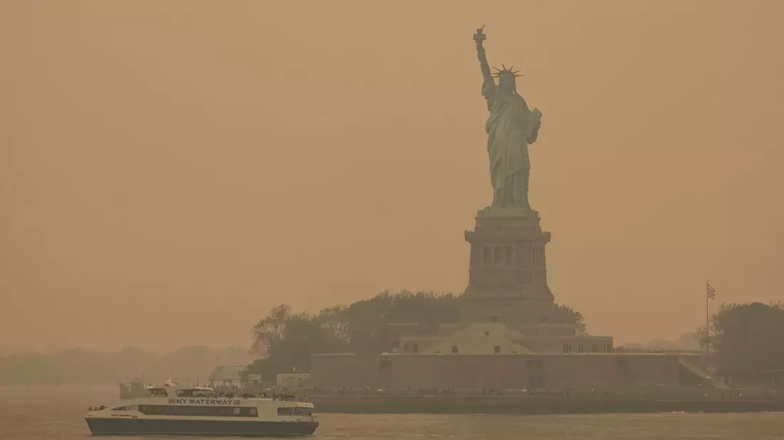 Die Freiheitsstatue ist in orangefarbenen Dunst gehüllt. - Bild: Yuki Iwamura/AP/dpa
