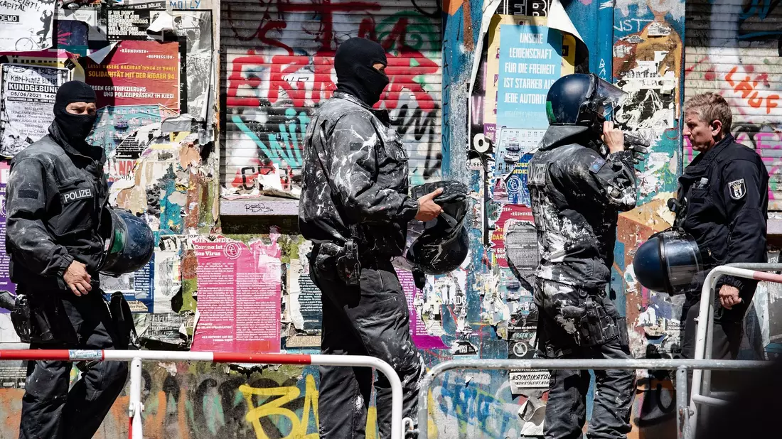 Mit Farbe beworfene Polizeibeamte verlassen das Haus Nr. 94 in der Rigaer Straße in Berlin. - Bild: Paul Zinken/dpa-Zentralbild/dpa