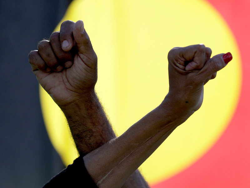 Ein Mann und eine Frau verschränken die Arme vor einer Aborigines-Flagge während einer Kundgebung der Bewegung «Black Lives Matter» in Sydney (Symbolbild). Der «Sydney Morning Herald» hat sich für seine Berichterstattung zum Myall-Creek-Massaker entschuldigt. - Foto: Rick Rycroft/AP/dpa