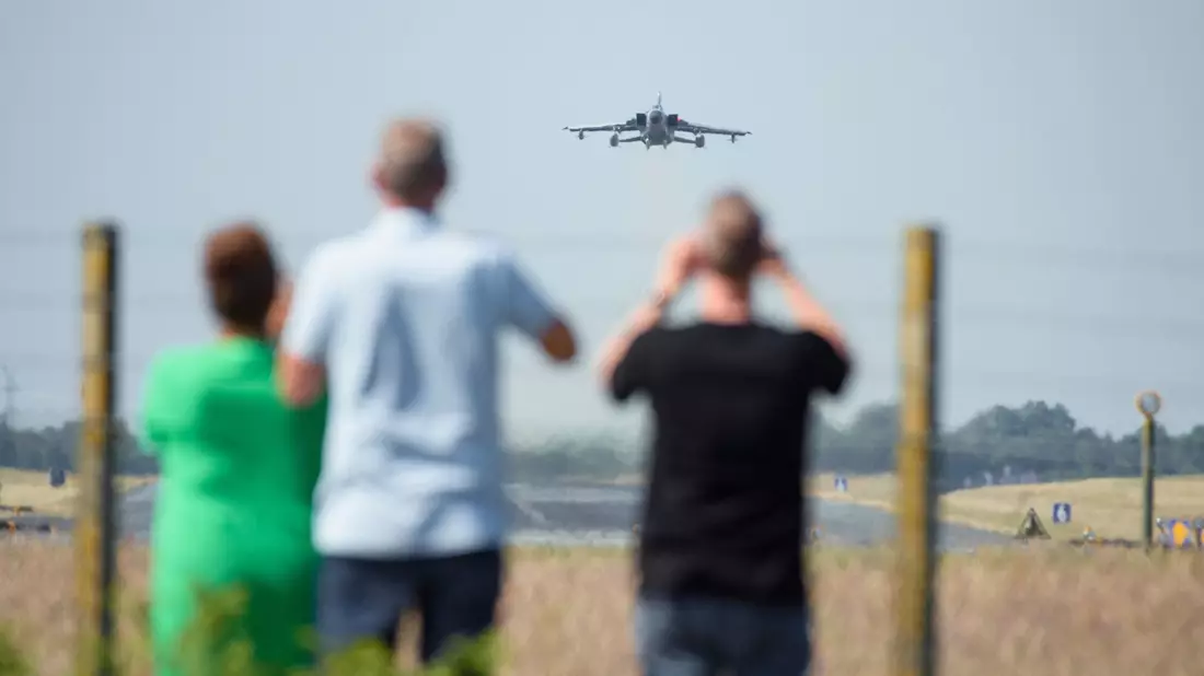 Schaulustige beobachten den Start eines Tornado-Kampfjets zu Beginn des internationalen Luftwaffen-Manövers «Air Defender 2023» am Zaun des Fliegerhorst Schleswig/Jagel. - Bild: Gregor Fischer/dpa