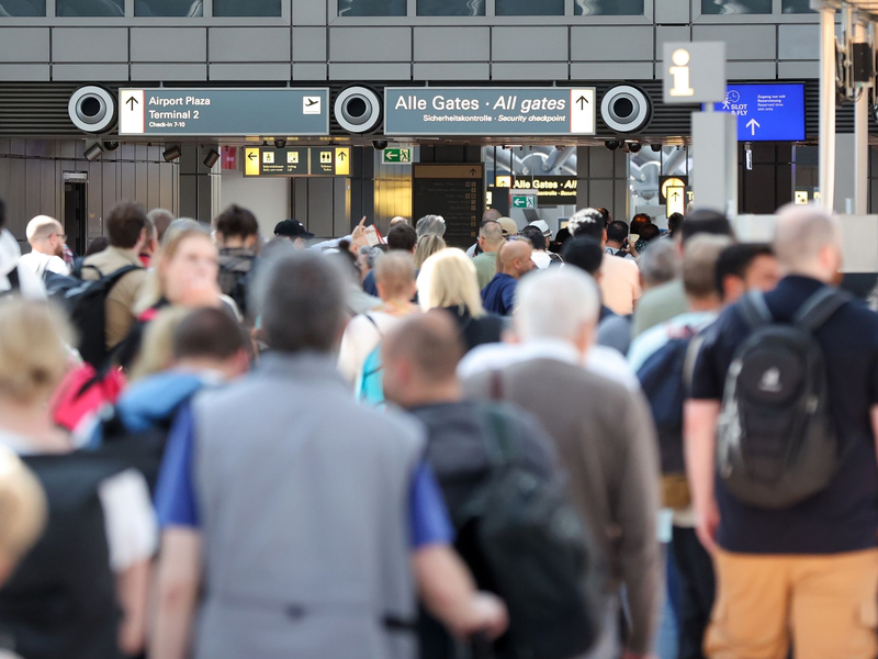 Reisende stehen in einer langen Schlange vor der Sicherheitskontrolle am Hamburger Flughafen an. - Foto: Bodo Marks/dpa