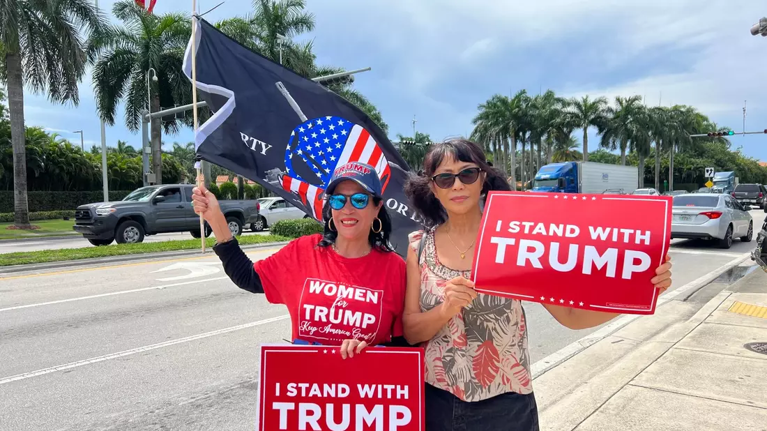 Zwei Trump-Anhängerinnen empfangen den Ex-Präsidenten vor seinem Hotel in Miami mit Schildern, auf denen «Ich stehe hinter Trump» geschrieben steht. - Bild: Magdalena Tröndle/dpa