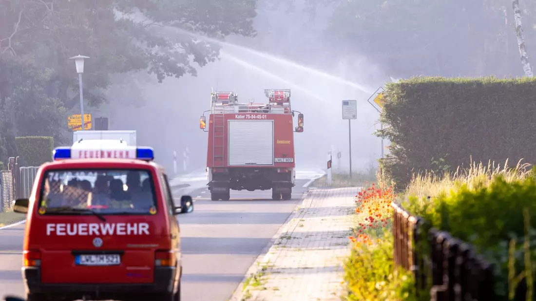 Feuerwehrfahrzeuge in der evakuierten Ortschaft Volzrade, durch die Rauch vom Waldbrand auf dem ehemaligen Truppenübungsplatz zieht. - Bild: Jens Büttner/dpa