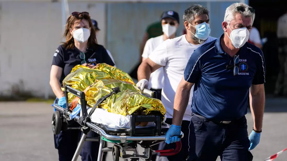 Sanitäter transportieren einen verletzten Überlebenden des Bootsunglücks zu einem Krankenwagen im Hafen der griechischen Stadt Kalamata. - Bild: Thanassis Stavrakis/AP/dpa
