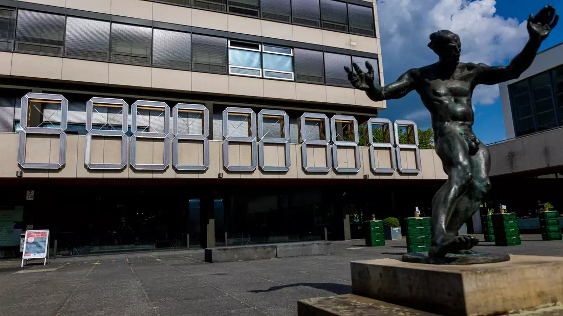 Eine «ClimateCrisisClock» hängt am Forumsgebäude der Technischen Universität (TU) Braunschweig hinter einer Dionysos-Skulptur. - Bild: Moritz Frankenberg/dpa