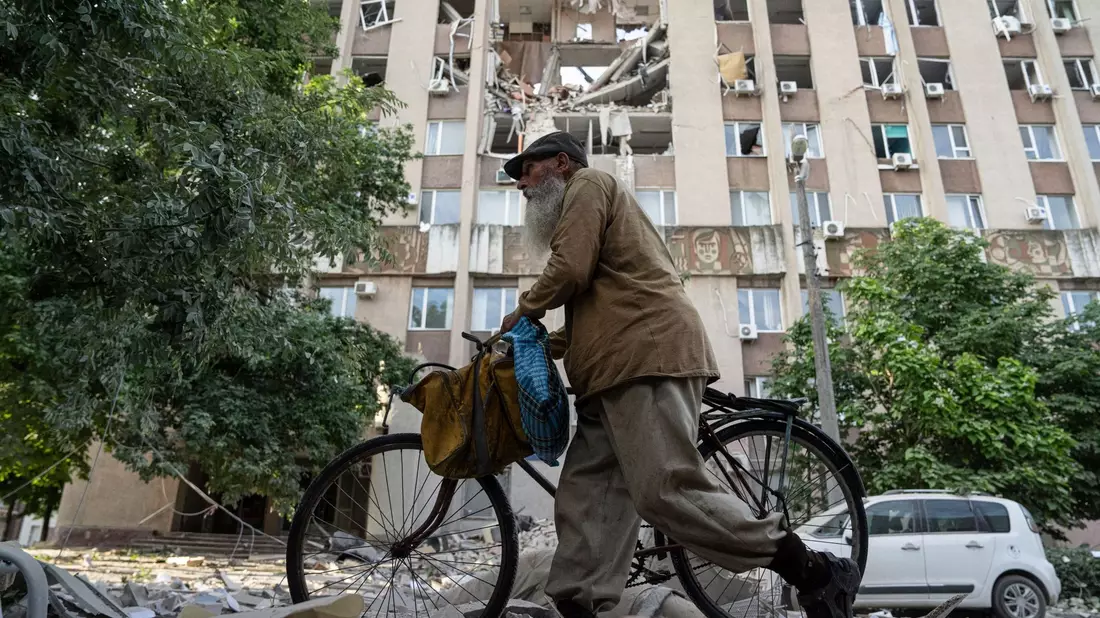 Ein Mann in Cherson schiebt sein Fahrrad vor einem Gebäude entlang, das durch einen Luftangriff schwer beschädigt wurde. - Bild: Evgeniy Maloletka/AP/dpa
