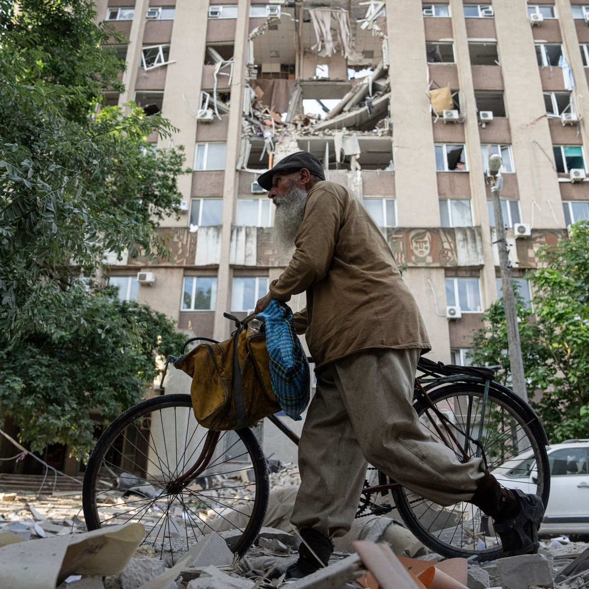 Ein Mann in Cherson schiebt sein Fahrrad vor einem Gebäude entlang, das durch einen Luftangriff schwer beschädigt wurde. - Foto: Evgeniy Maloletka/AP/dpa