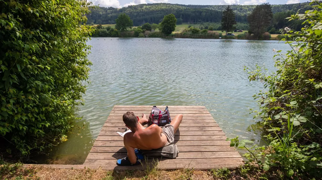 Ein Mann genießt die Sonne am Badesee Plüderhausen - und vielleicht auch den ein oder anderen Sommerhit. - Bild: Christoph Schmidt/dpa