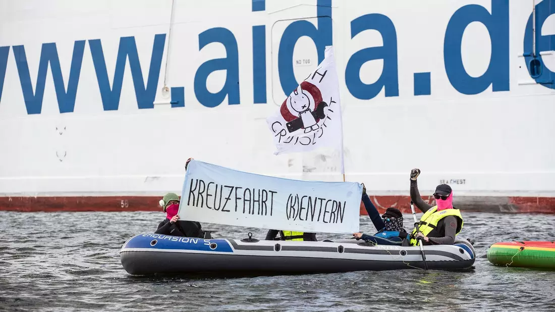 Neben der «Aida Diva» halten Klimaaktivisten ein Transparent mit der Aufschrift «Kreuzfahrt (K)entern». - Bild: Frank Hormann/dpa
