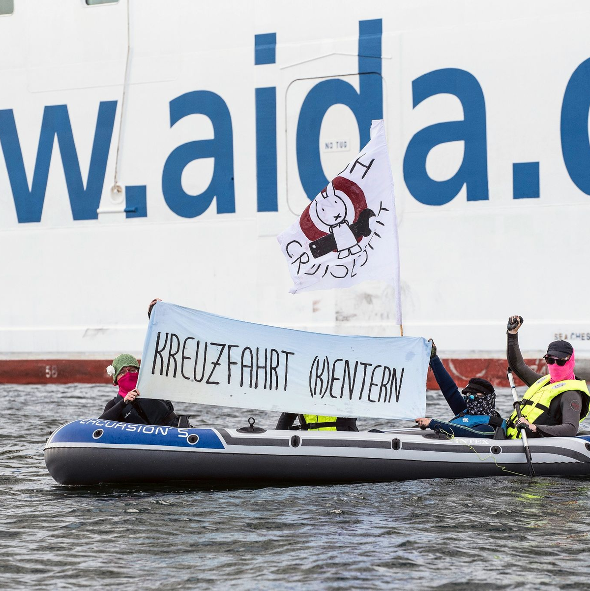 Neben der «Aida Diva» halten Klimaaktivisten ein Transparent mit der Aufschrift «Kreuzfahrt (K)entern». - Foto: Frank Hormann/dpa