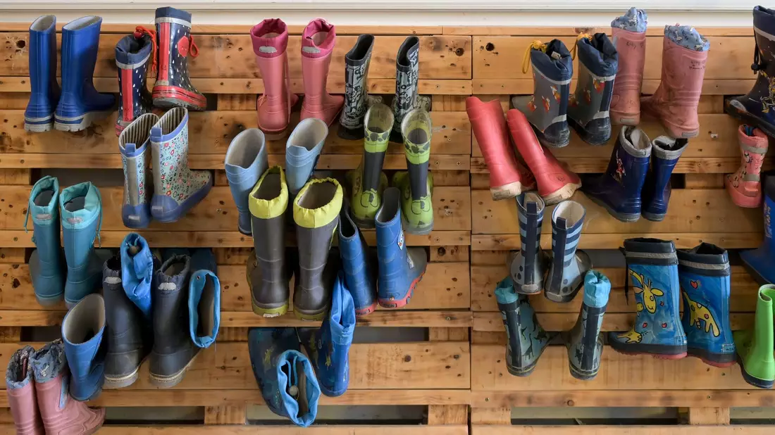 Gummistiefel hängen an der Palettenwand einer Kindertagesstätte in Halle (Saale). In Deutschland fehlen Erzieherinnen und Erzieher. - Bild: Heiko Rebsch/dpa