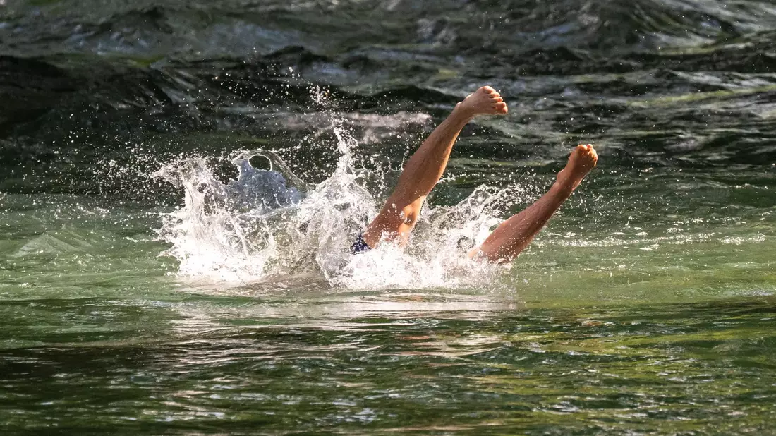 Ein junger Mann erfrischt sich mit einem Sprung in den Eisbach im Englischen Garten in München. - Bild: Peter Kneffel/dpa