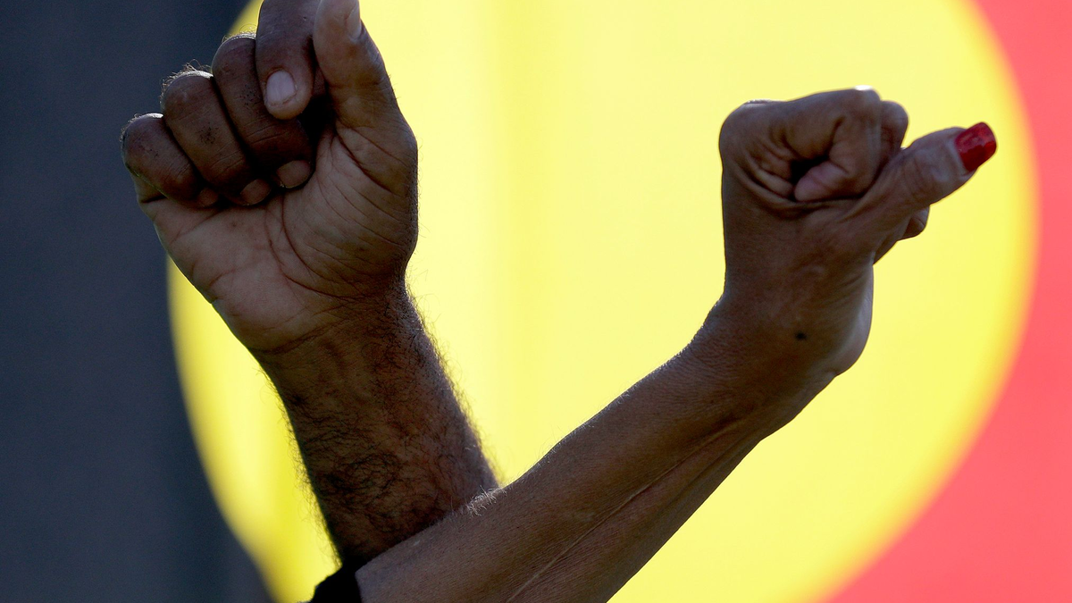 Während einer Kundgebung in Sydney verschränken  zwei Demonstranten vor einer Aborigine-Flagge ihre Arme. - Foto: Rick Rycroft/AP/dpa