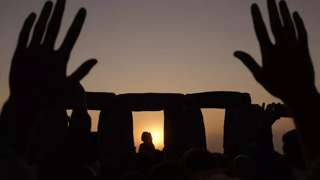 Menschen versammeln sich bei Sonnenaufgang am Tag der Sommersonnenwende um den Heel Stone in Stonehenge. - Bild: Kin Cheung/AP
