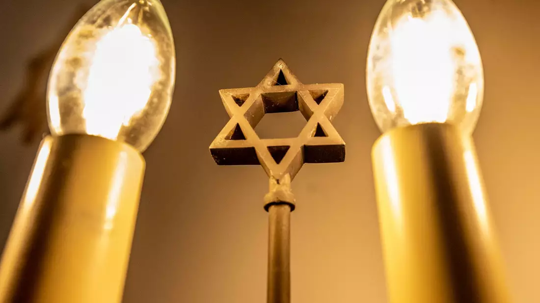Ein siebenarmiger Leuchter (Menora) mit einem Davidstern in der Mitte leuchtet in einer Synagoge. Fragen zum Judentum werden auf einer Website beantwortet. - Bild: David Inderlied/dpa